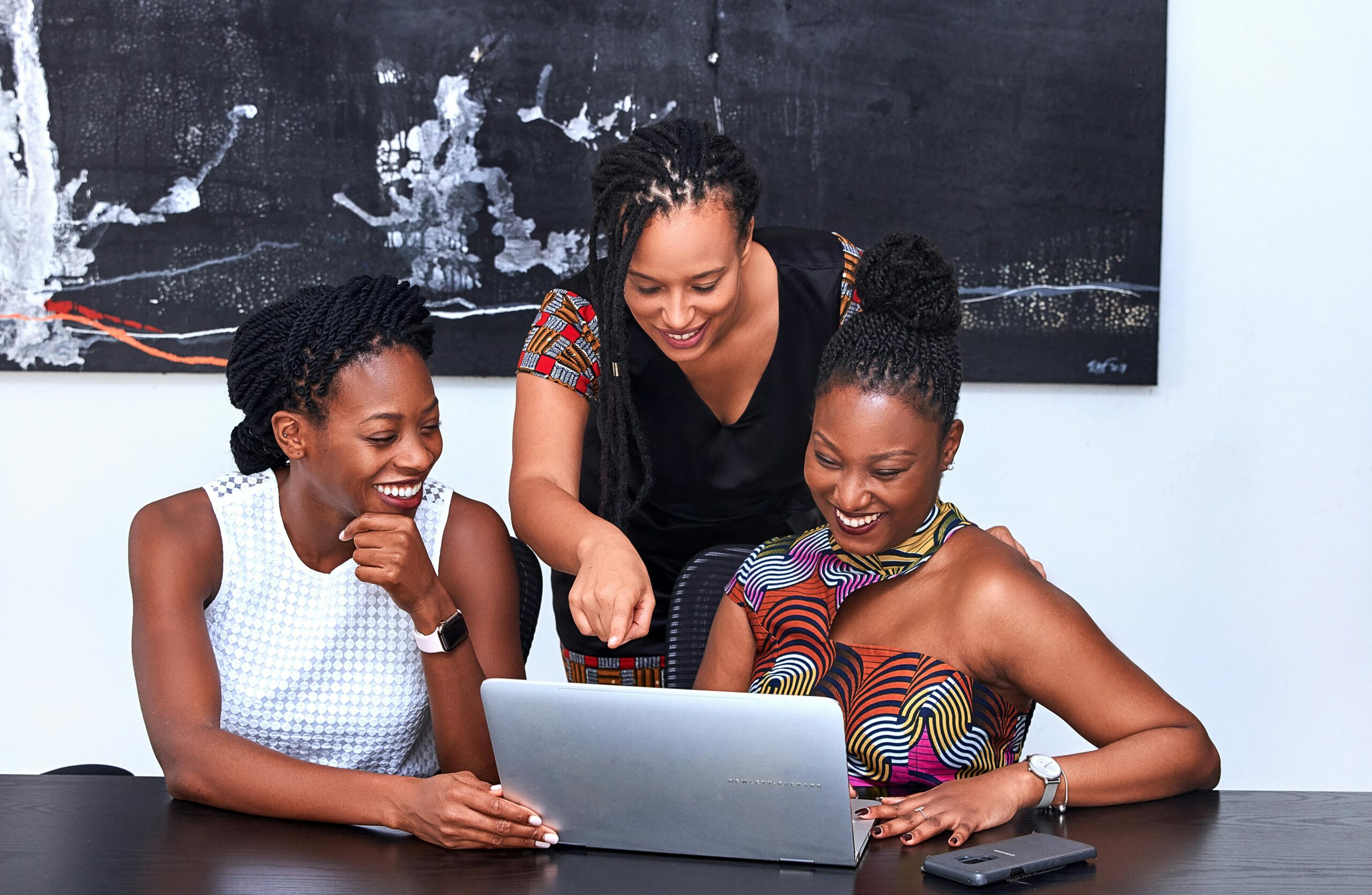 Three African American women collaborating at a laptop, focused and happy during a meeting indoors.